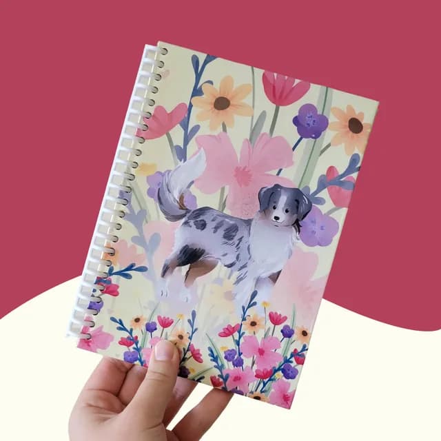 Carnet A5 à spirale tenu en main, illustré d'un berger australien entouré de fleurs colorées